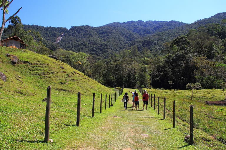 Caminho de terra entre o pasto e uma cerca de madeira, com a serra ao fundo, no Vale do Alcantilado, em Bocaina de Minas, Visconde de Mauá