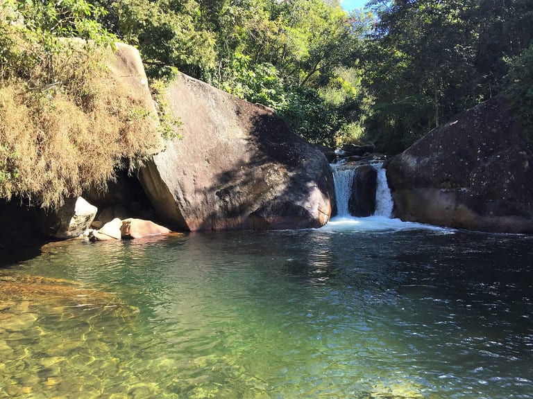 Poção da Maromba com água transparente, pedras grandes e a pequena queda ao fundo, na Vila da Maromba, em Visconde de Mauá