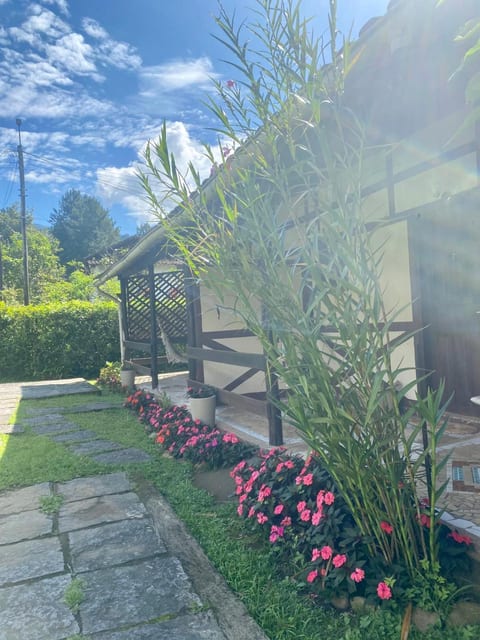 Fachada de um chalé da Pousada do Figa, com varanda, rede e flores no jardim, em Visconde de Mauá