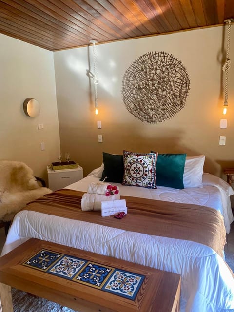 Cama queen de um chalé com lareira da Pousada do Figa, com almofadas coloridas e toalhas