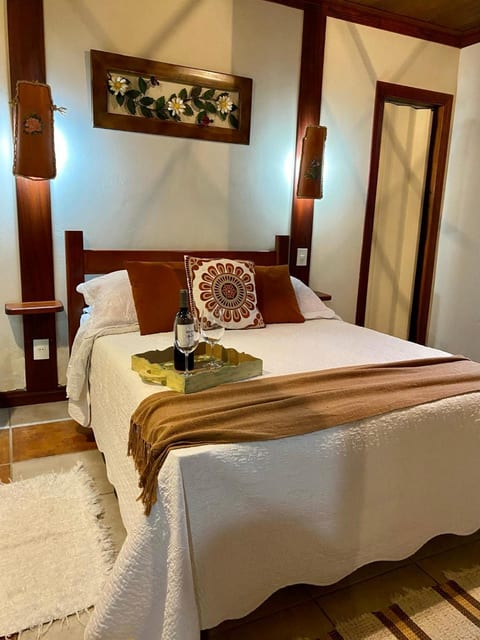 Suíte da Pousada do Figa com cama de casal, manta terracota e bandeja de espumante de boas-vindas