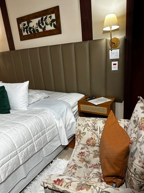 Cama king e poltrona florida com almofada caramelo na Suíte 2 da Pousada do Figa