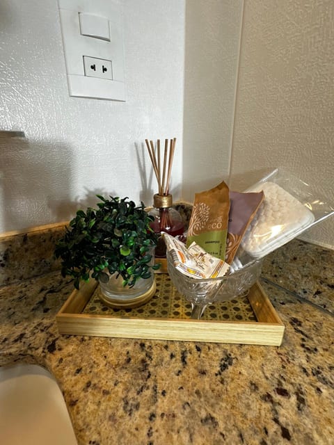 Bandeja de palhinha com difusor de aromas, planta e kit de higiene no banheiro da Suíte 2 da Pousada do Figa