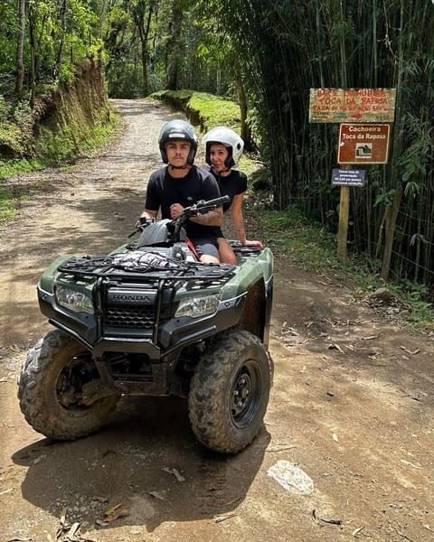 Casal num passeio de quadriciclo por estrada de terra entre bambus, em Visconde de Mauá